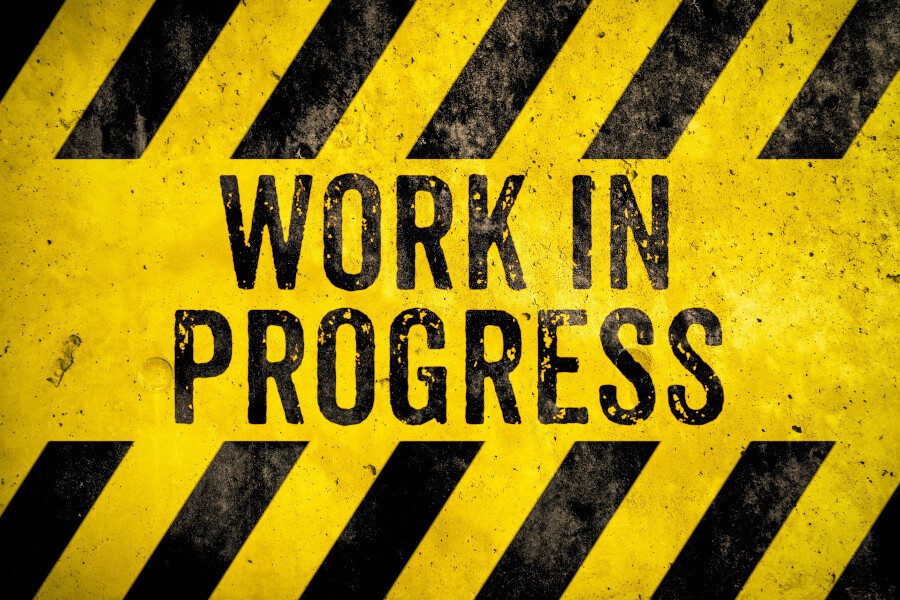 Work in progress warning sign text with yellow and black stripes Work in progress warning sign text with yellow and black stripes painted over concrete wall cement texture background. Concept for do not enter the area, caution, danger, construction site.